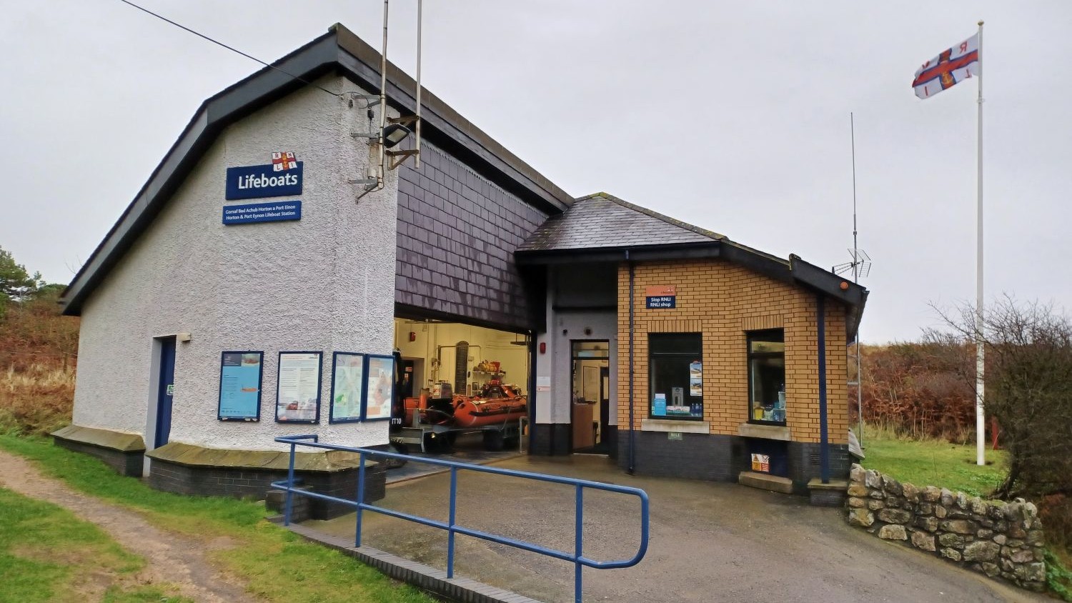 A one storey white building with a sloping roof and a yellow brick shop on the side.