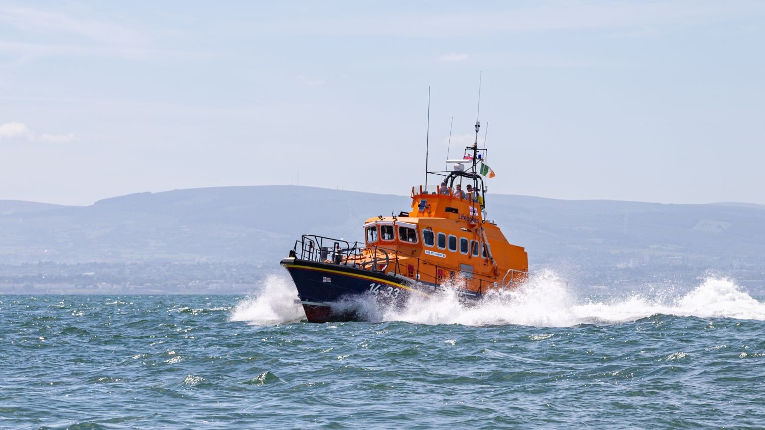 A Trent class all weather lifeboat creating white spray on choppy blue water.