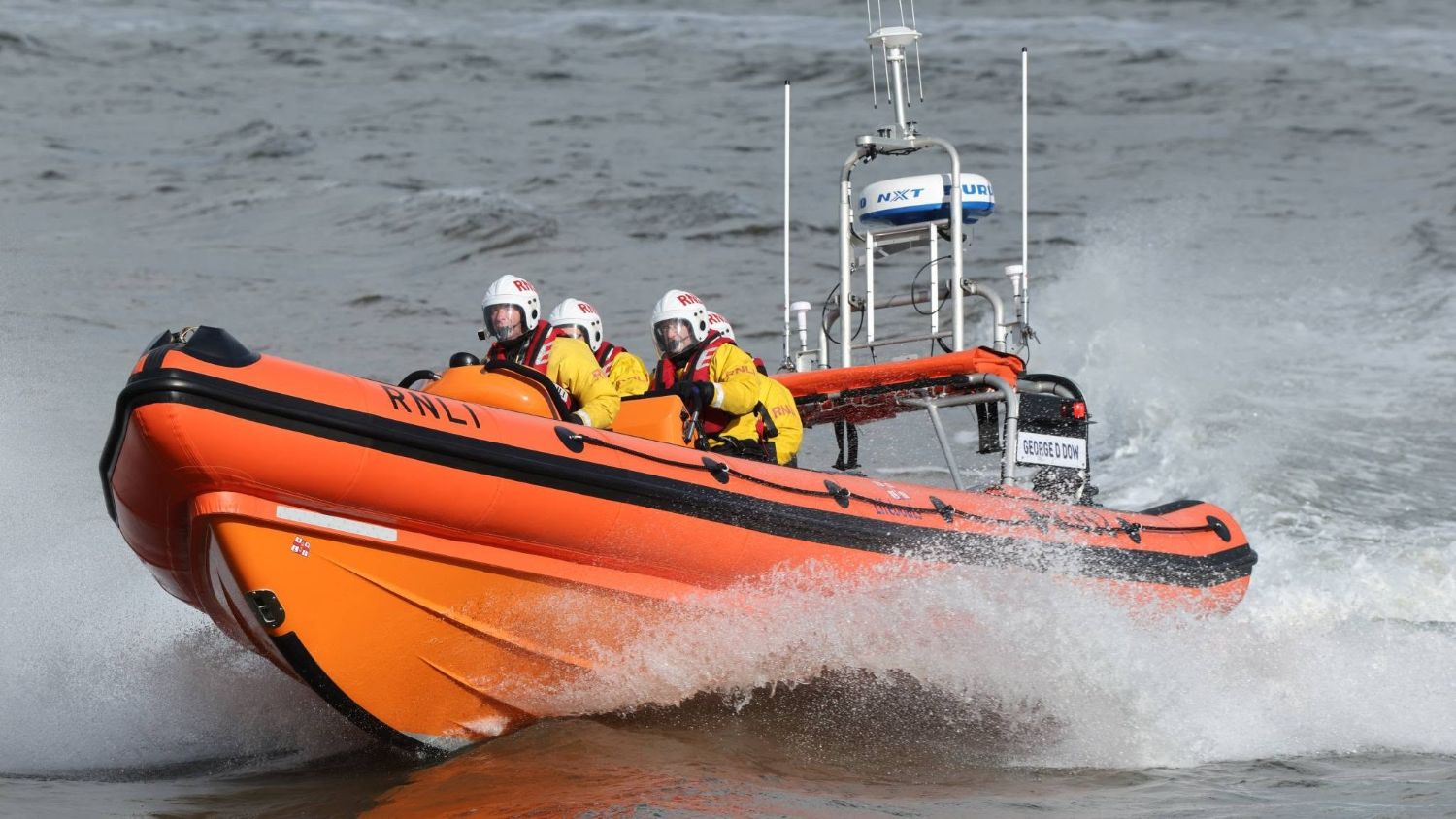 RNLI B class lifeboat George D Dow powering through choppy water with three crew members wearing RNLI helmets and protective clothing on board.
