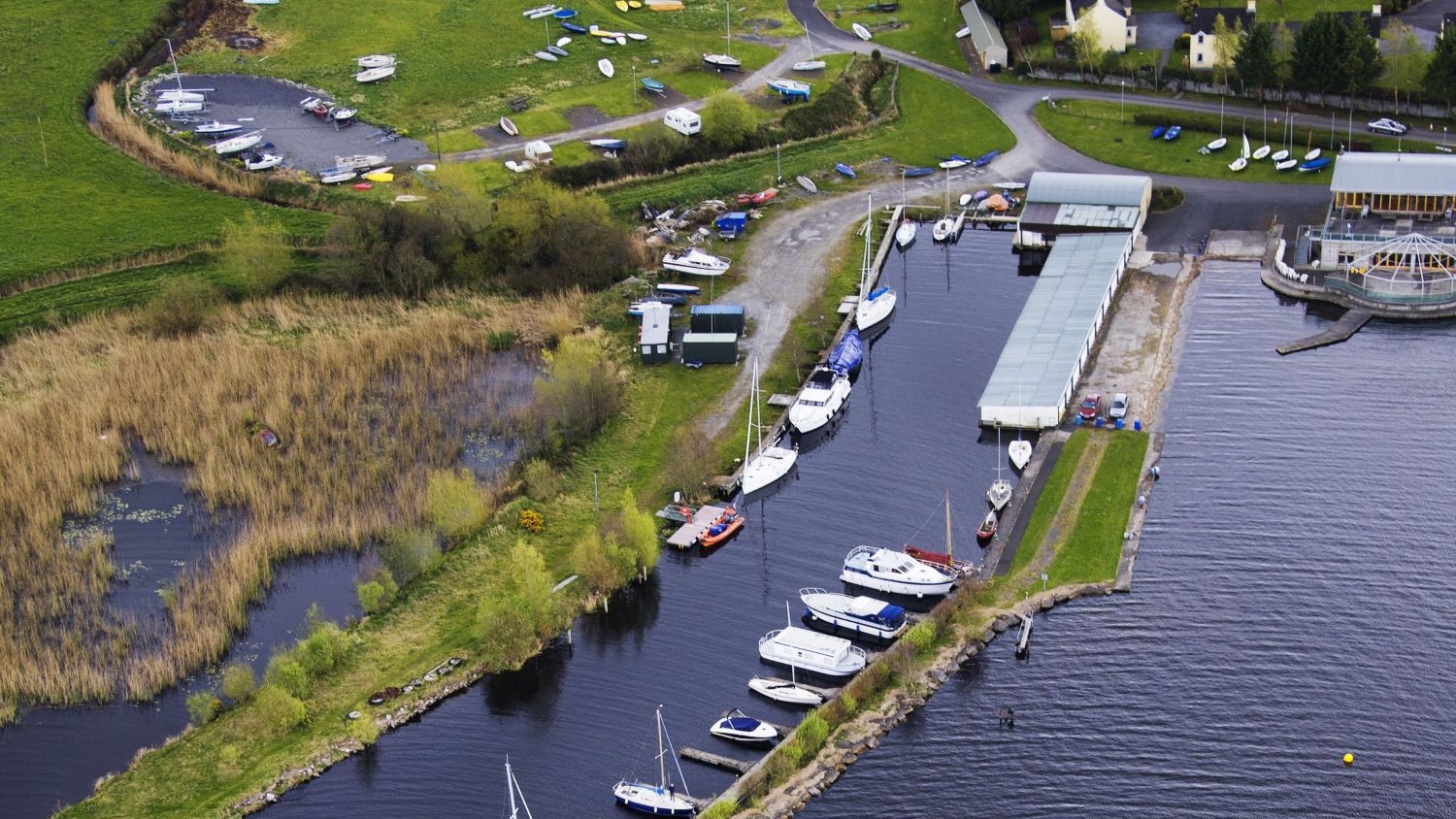 A long grey building with a narrow sea wall where sailing boats are moored.