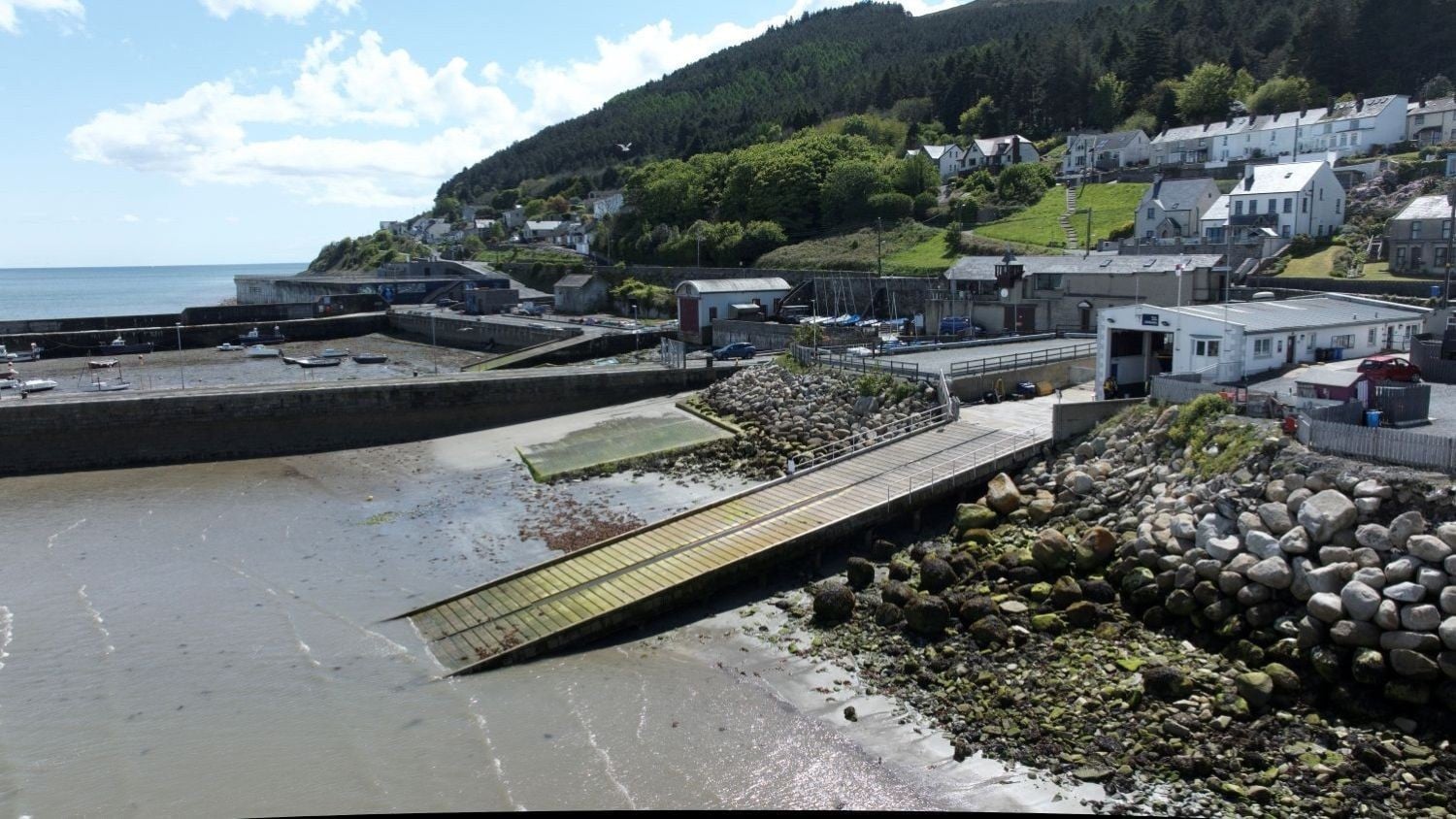 A one storey white building with a long slipway. Rows of houses and forest rise behind the station.