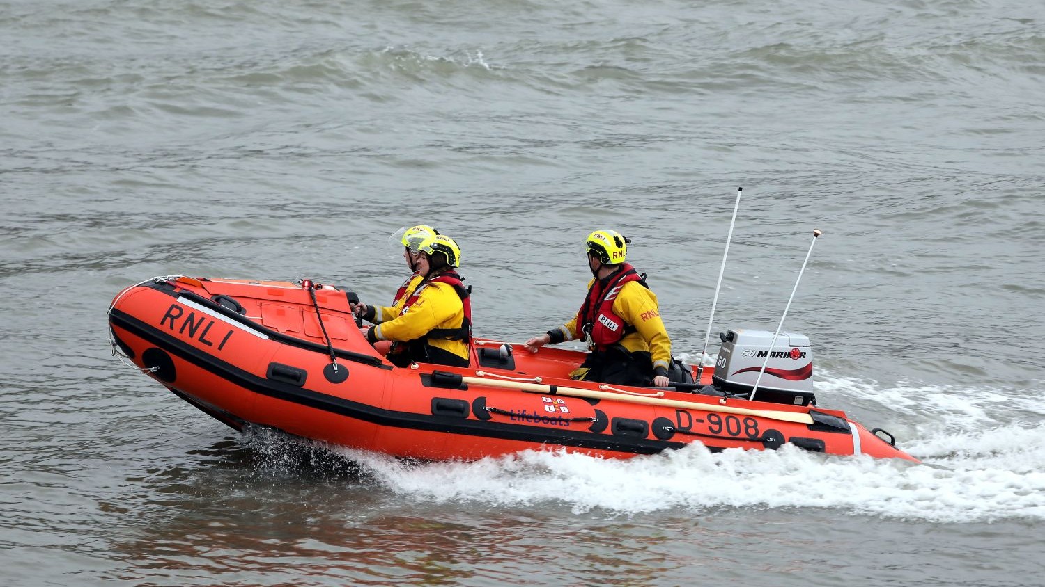 A small rib with three crew members on board on grey water.