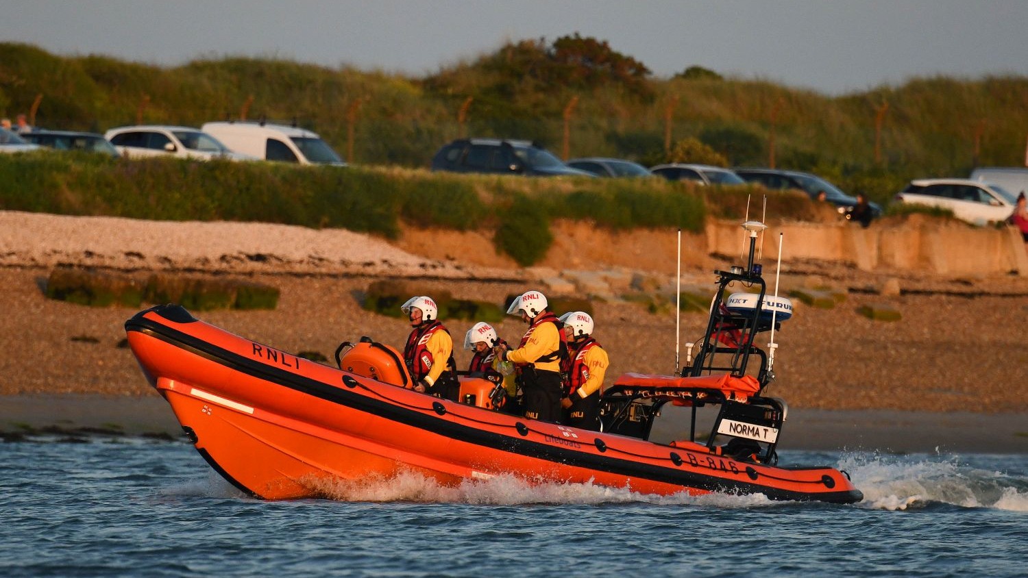 A large rib with four crew on calm water.