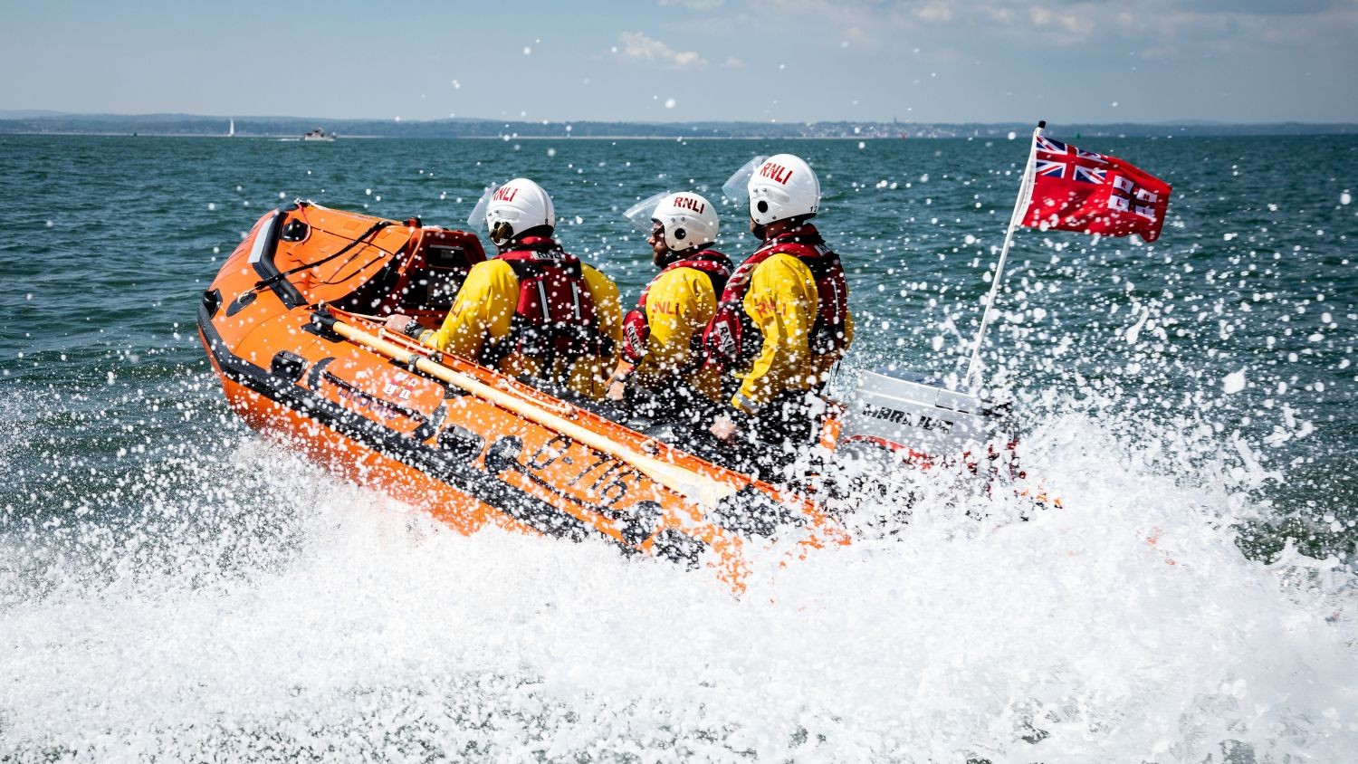 A small rib with three crew on blue water with lots of white spray.