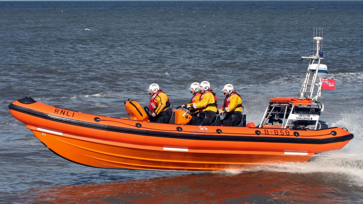 A large rib with four crew flies over calm grey water.