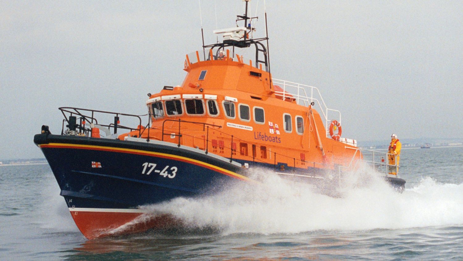 An orange RNLI lifeboat with crew on deck speeding across the water, creating sea spray.