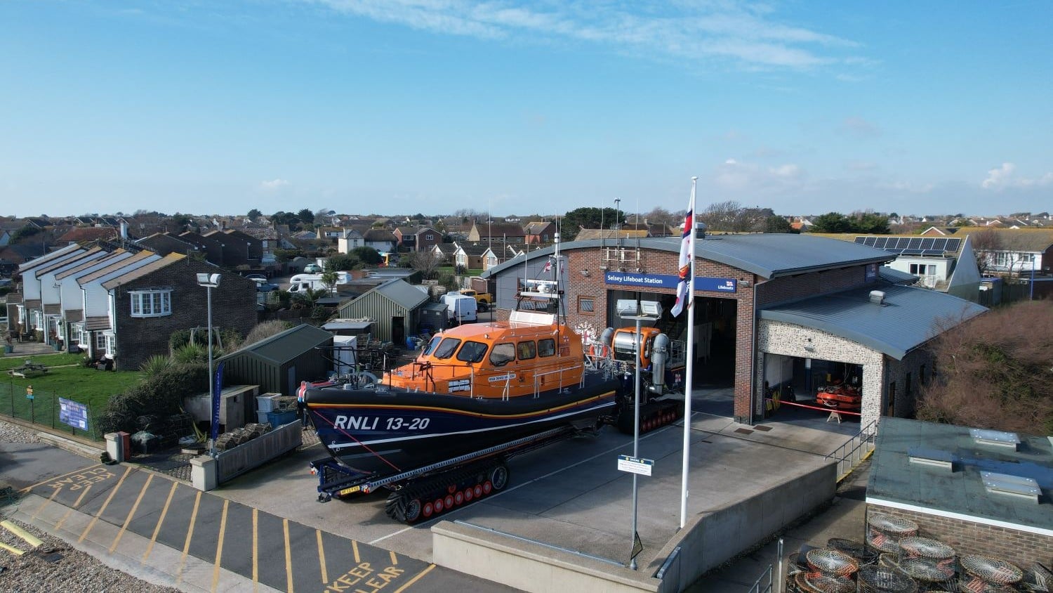 A red brick and grey building with curved roof and a shannon class all weather lifeboat emerging from the boatshed.
