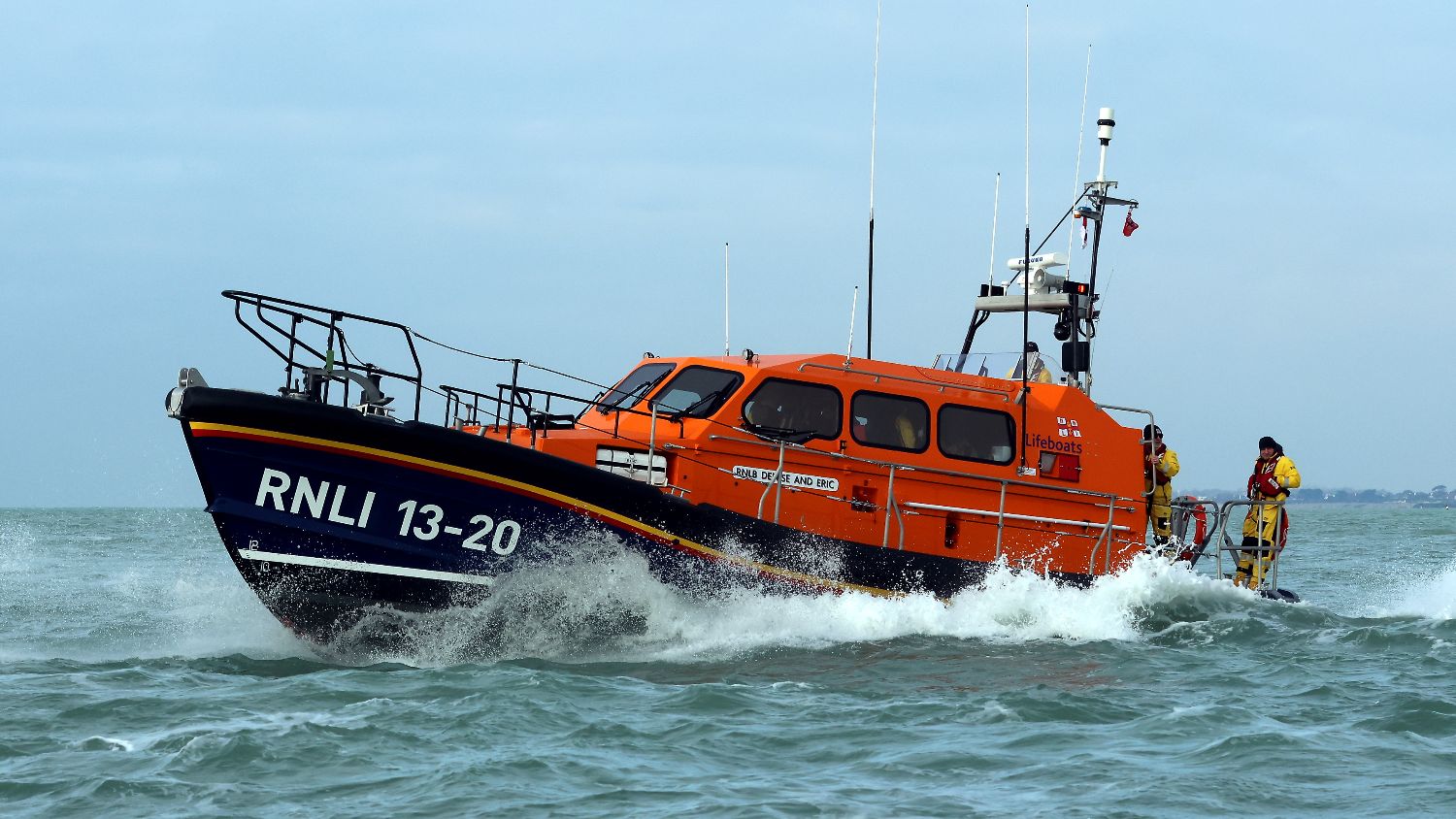 RNLI lifeboat RNLI number 13‑20 travelling at speed through choppy sea, with white spray breaking over the bow and crew visible on deck.