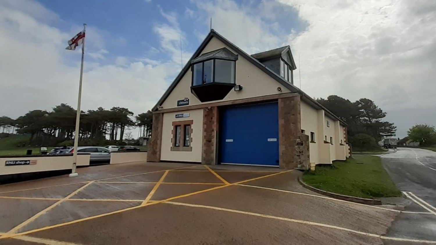 A two-storey cream building with a pointy roof and large blue boathouse door.
