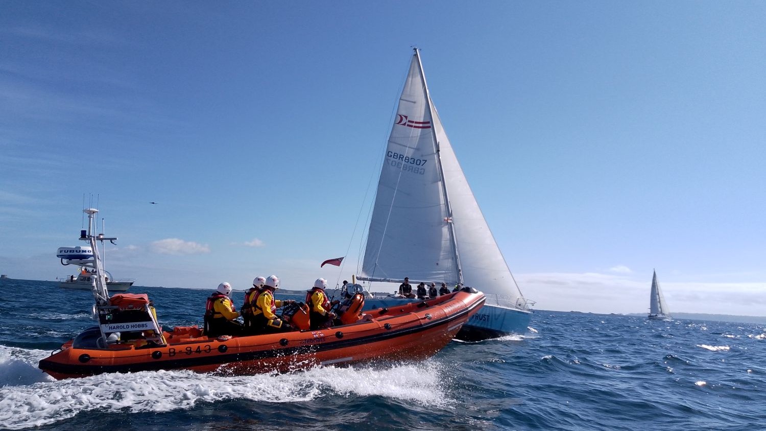 A large RIB with four crew onboard passes a sailing yacht under blue skies.