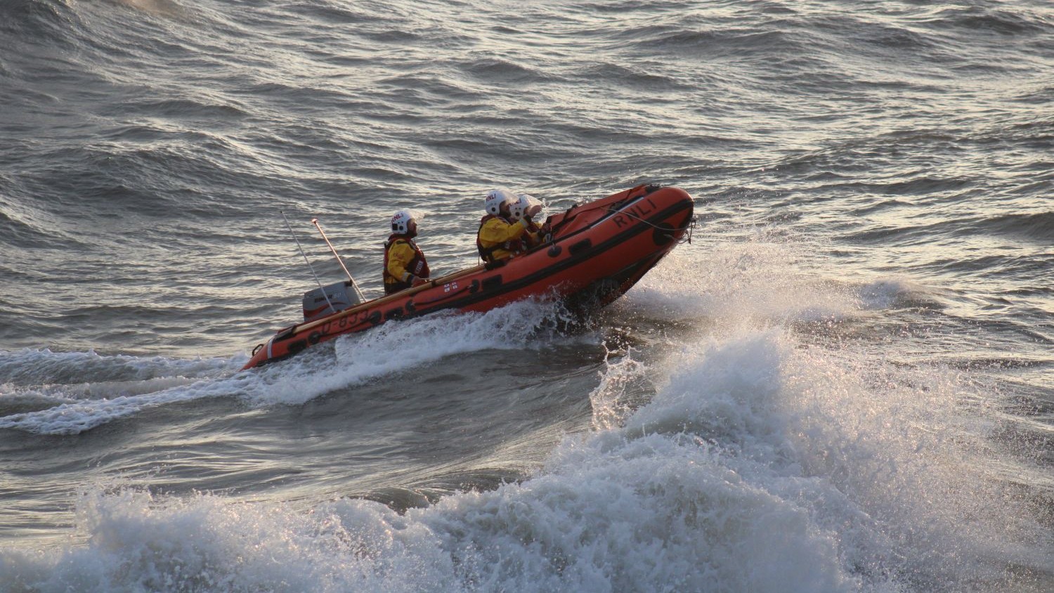 A small rib with three crew onboard in large grey waves.