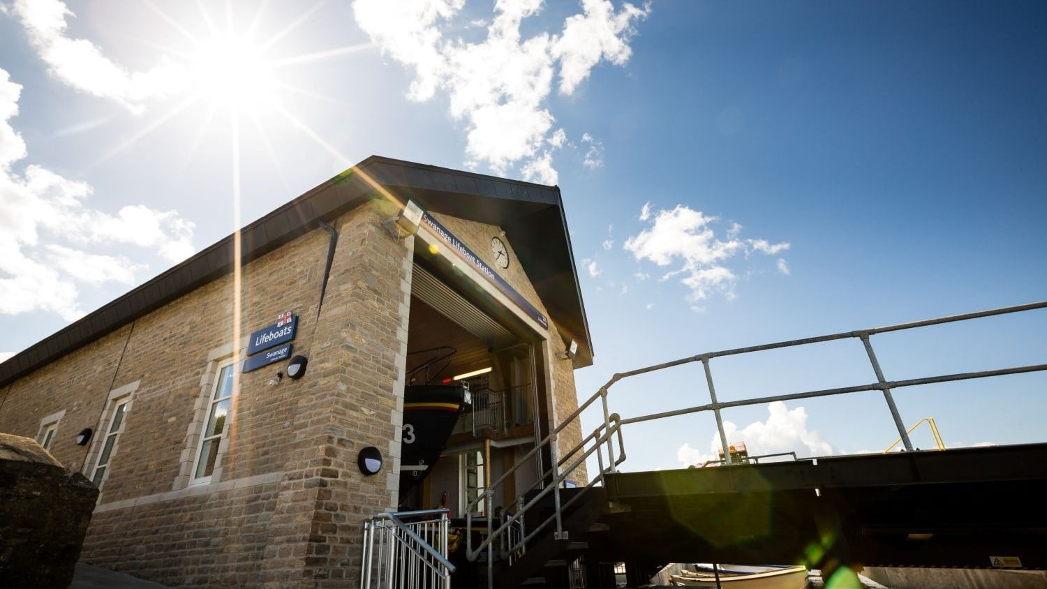 A tall single storey brick building with long windows. The lifeboat is just visible through an open door from the slipway.