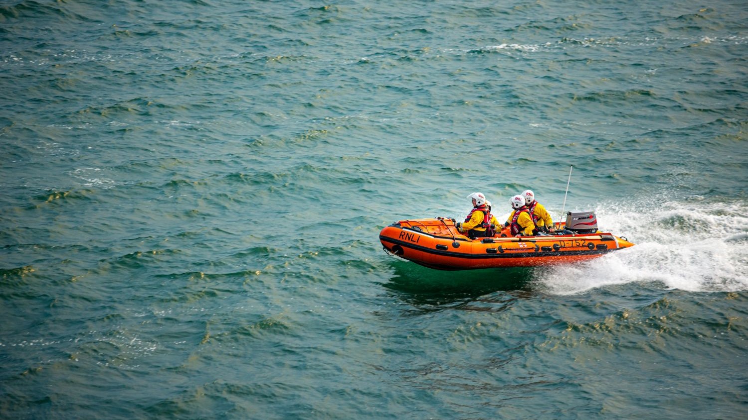 A small orange rib with four crew skating over green waves.