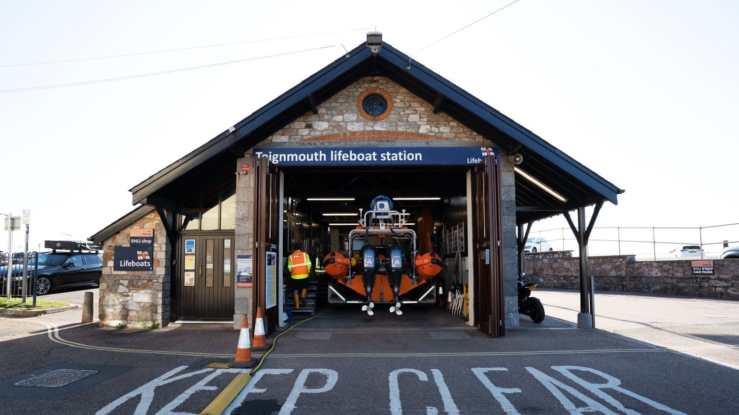 A one-storey stone building with pointy roof and open boatshed doors showing an inshore lifeboat.