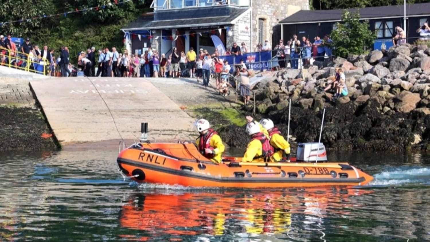 Torbay's D Class lifeboat underway in the harbour with Torbay Lifeboat Station in the background.