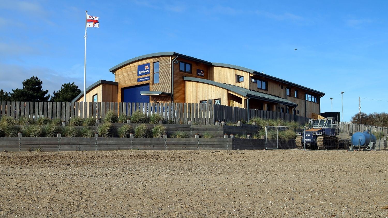 A two-storey wooden building with curved rooves and large blue doors to the boatshed.