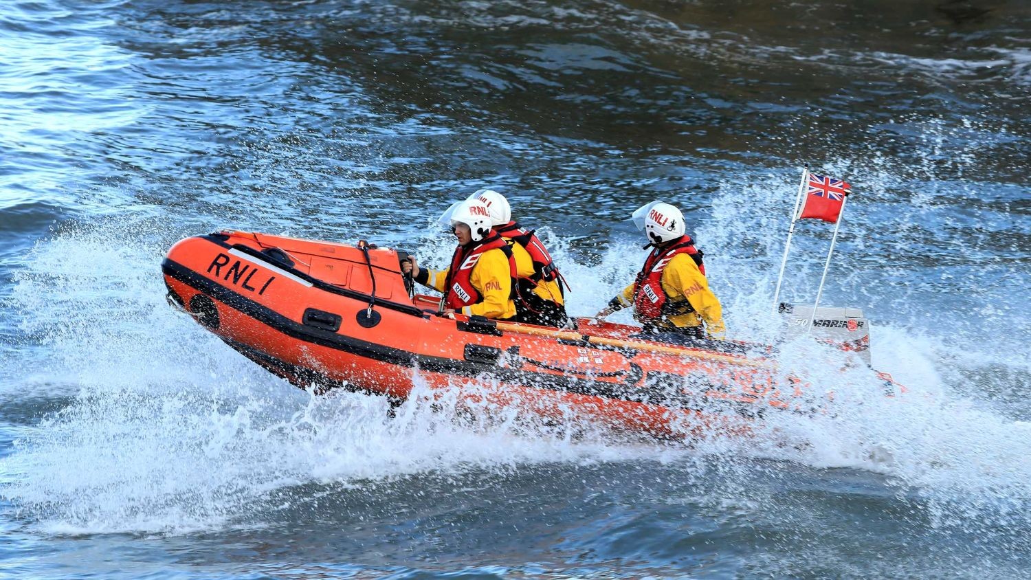 A small rib with three crew cresting a wave with lots of spray.