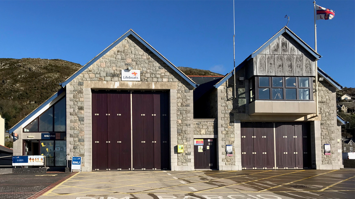 A shop front with large brown doors with a high sea cliff behind.
