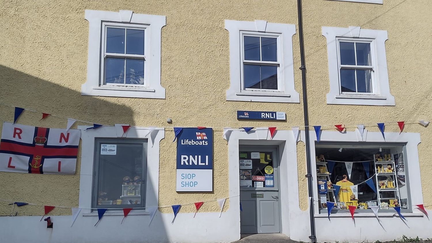 Shop front on a yellow building, adorned with flags and bunting.