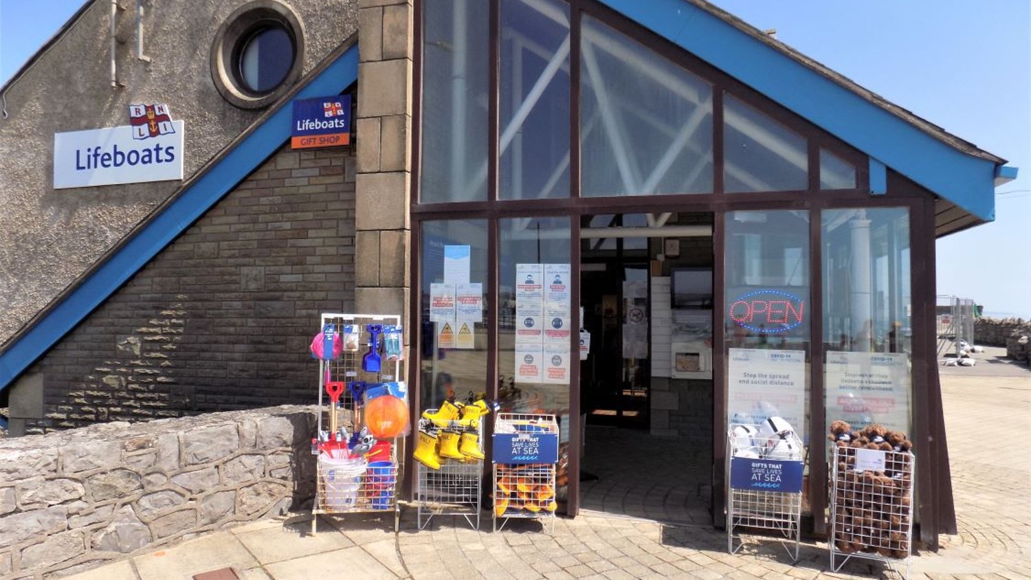 Porthcawl Lifeboats Gift Shop with white RNLI Lifeboats sign on the wall and stands of beachware and yellow wellies