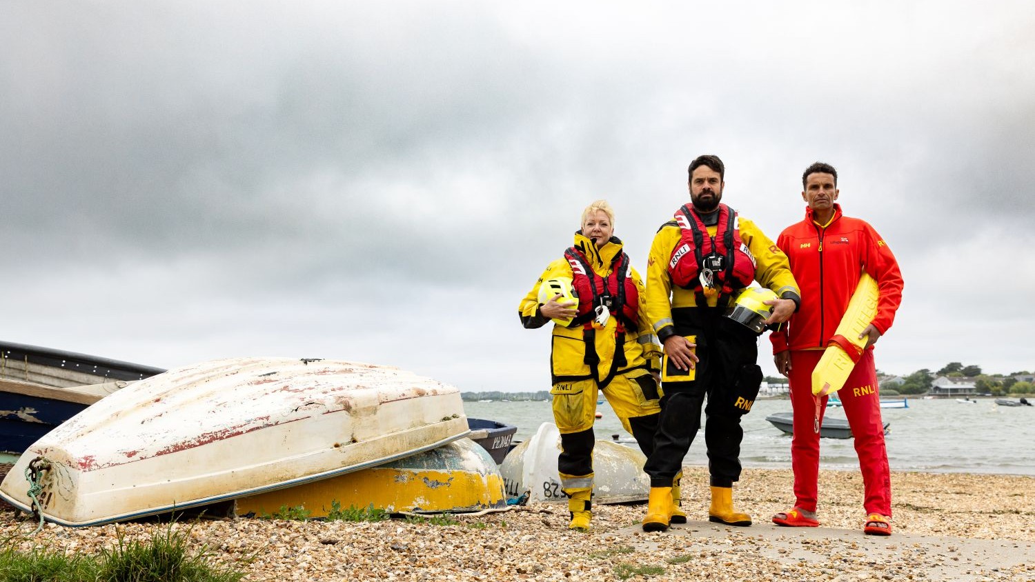 A lifeguard, an inshore lifeboat crew member and an all-weather lifeboat crew member stood on a shingle beach.