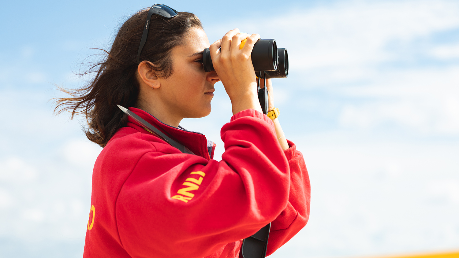 Lifeguard Jade Skilton monitoring the beach using a pair of binoculars at Sandbanks in Poole