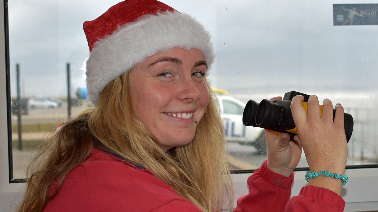 An RNLI lifeguard wearing a red Santa hat while keeping watch on Crosby Beach 