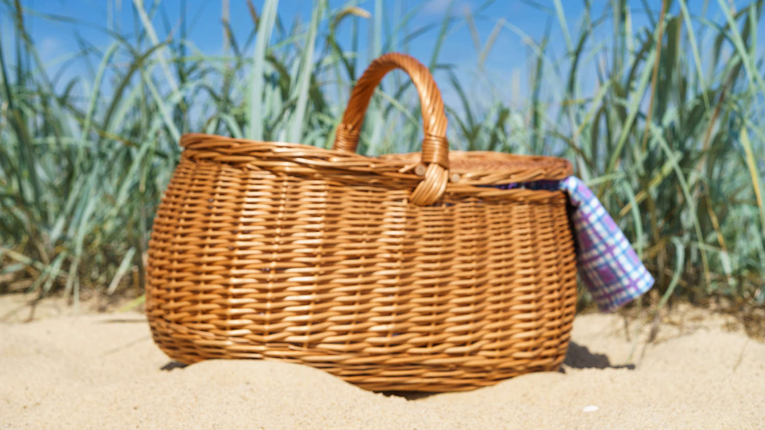 An enticing picnic hamper rests on the sand in the sunshine