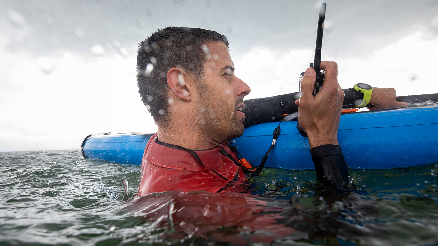 A paddleboarder clings onto their board, holding a handheld VHF