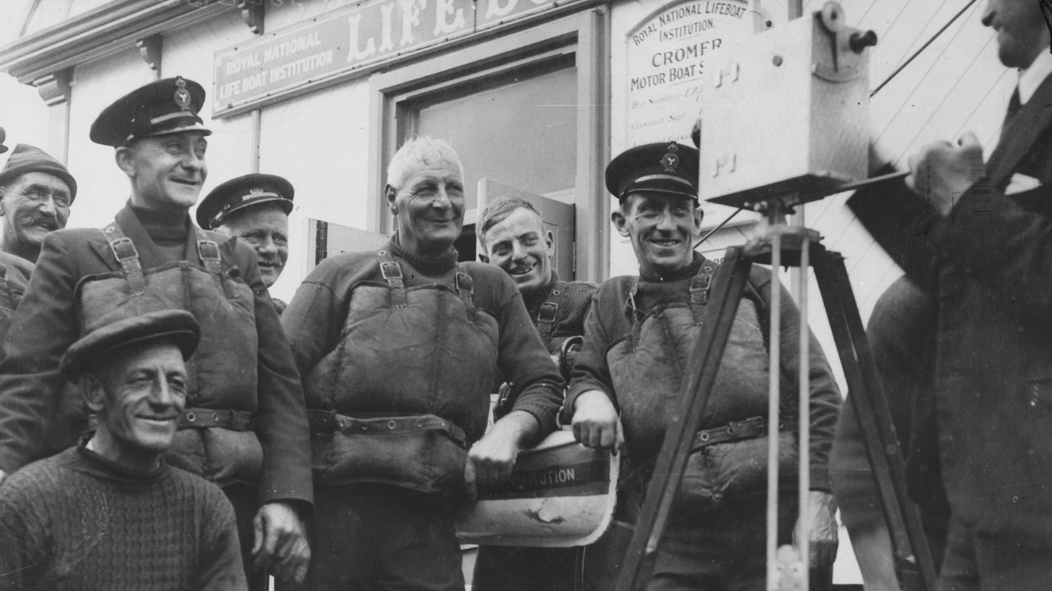 Black and white photo of a lifeboat crew with a film camera
