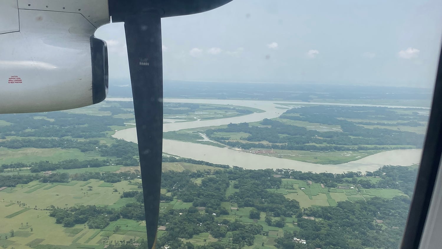 The view of Barisal from a plane, showing a large, winding river and lots of green fields