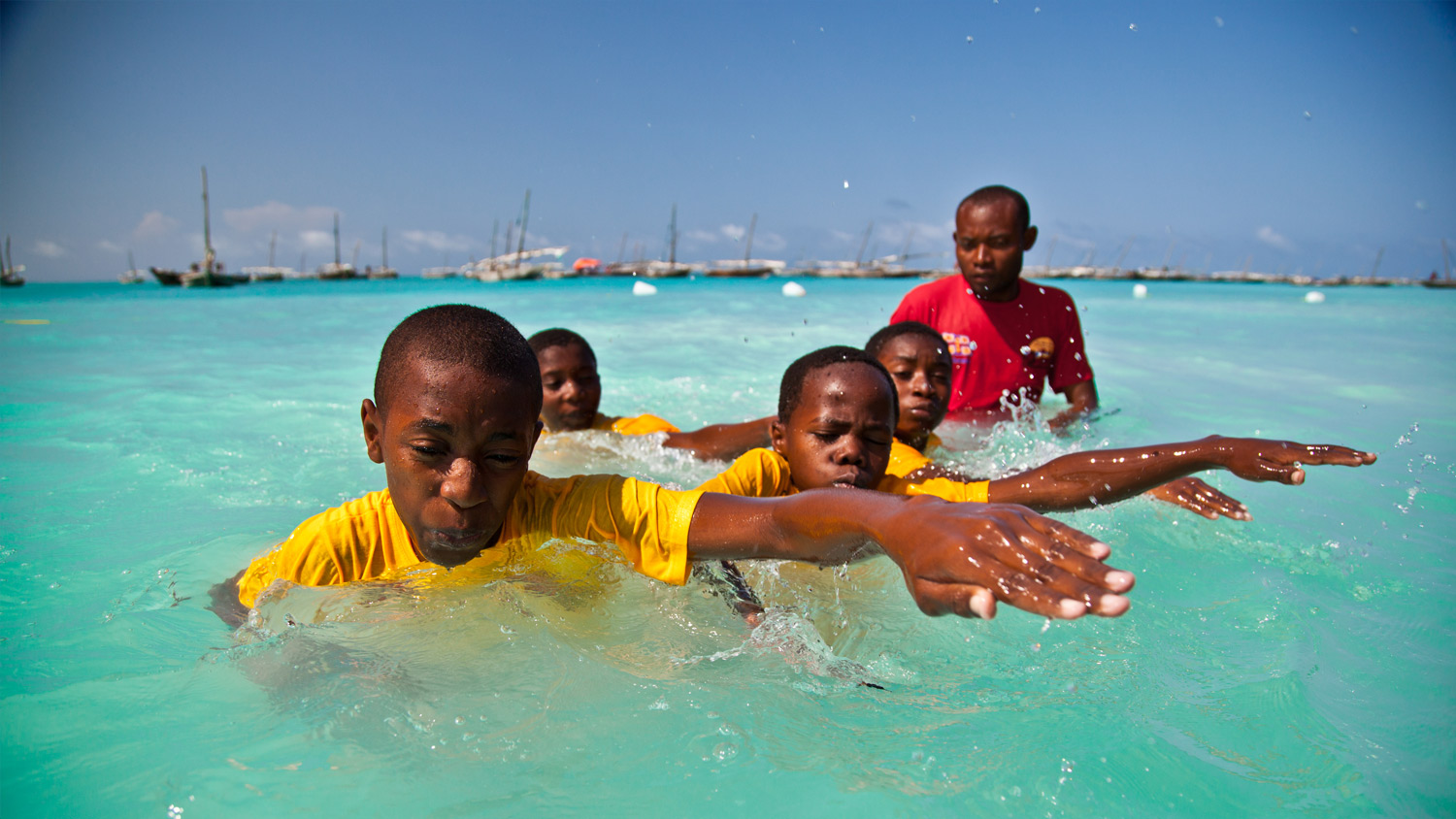 Four children swim in front of an adult swim teacher