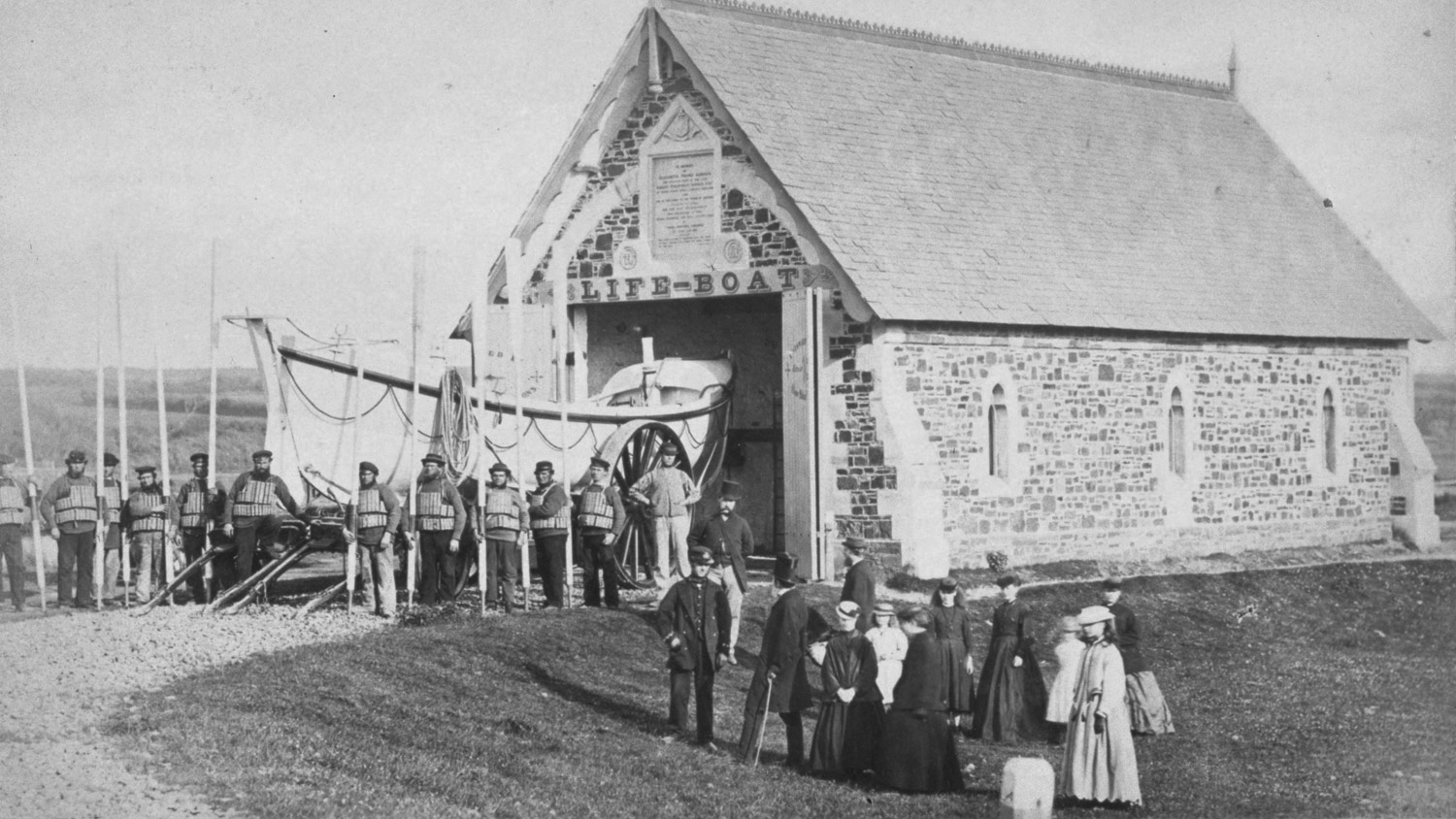 Black and white image of lifeboat station, lifeboat crew and guests in Victorian garb