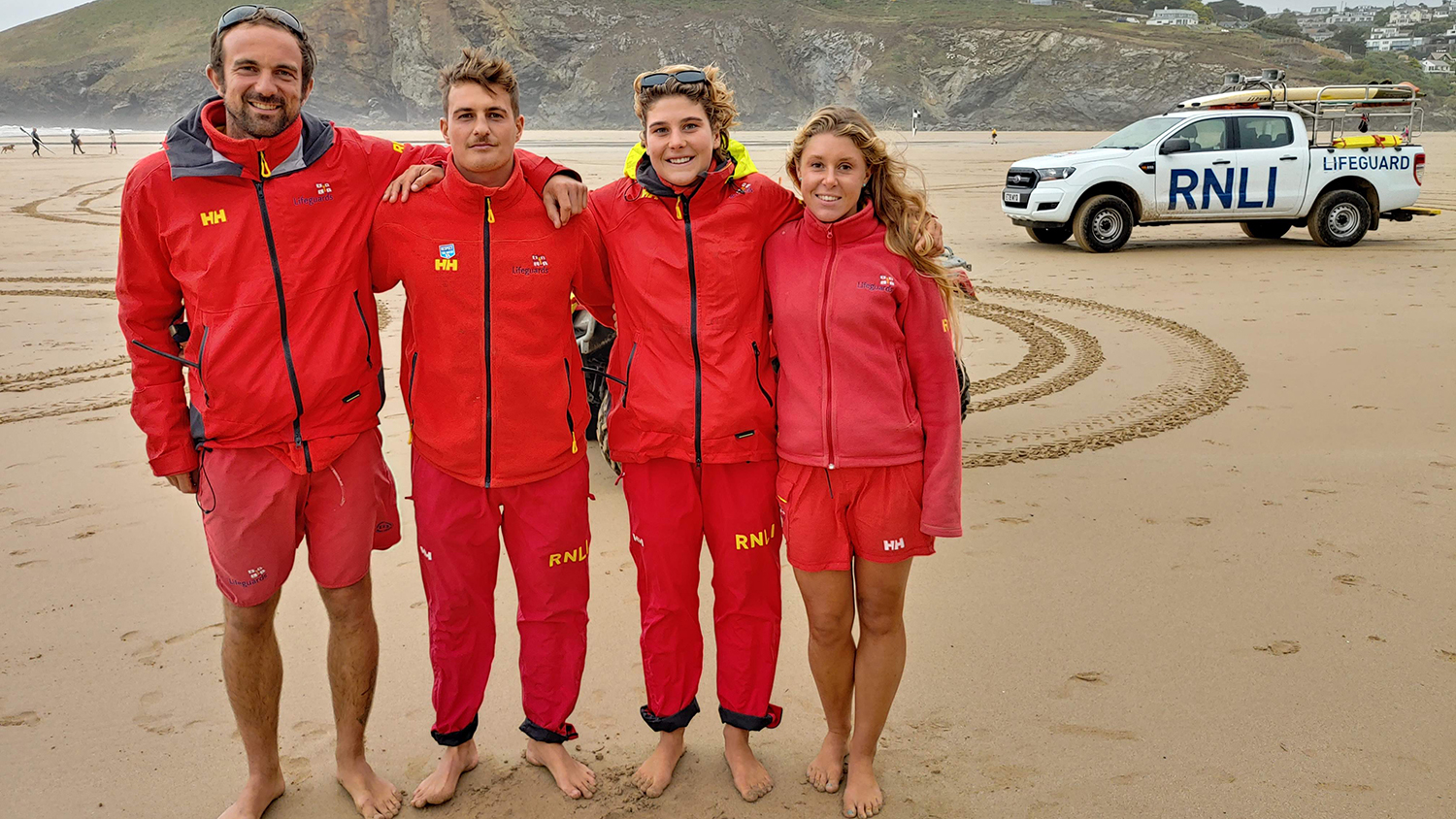 The lifeguards who saved Jon's life stand on the sand, smiling