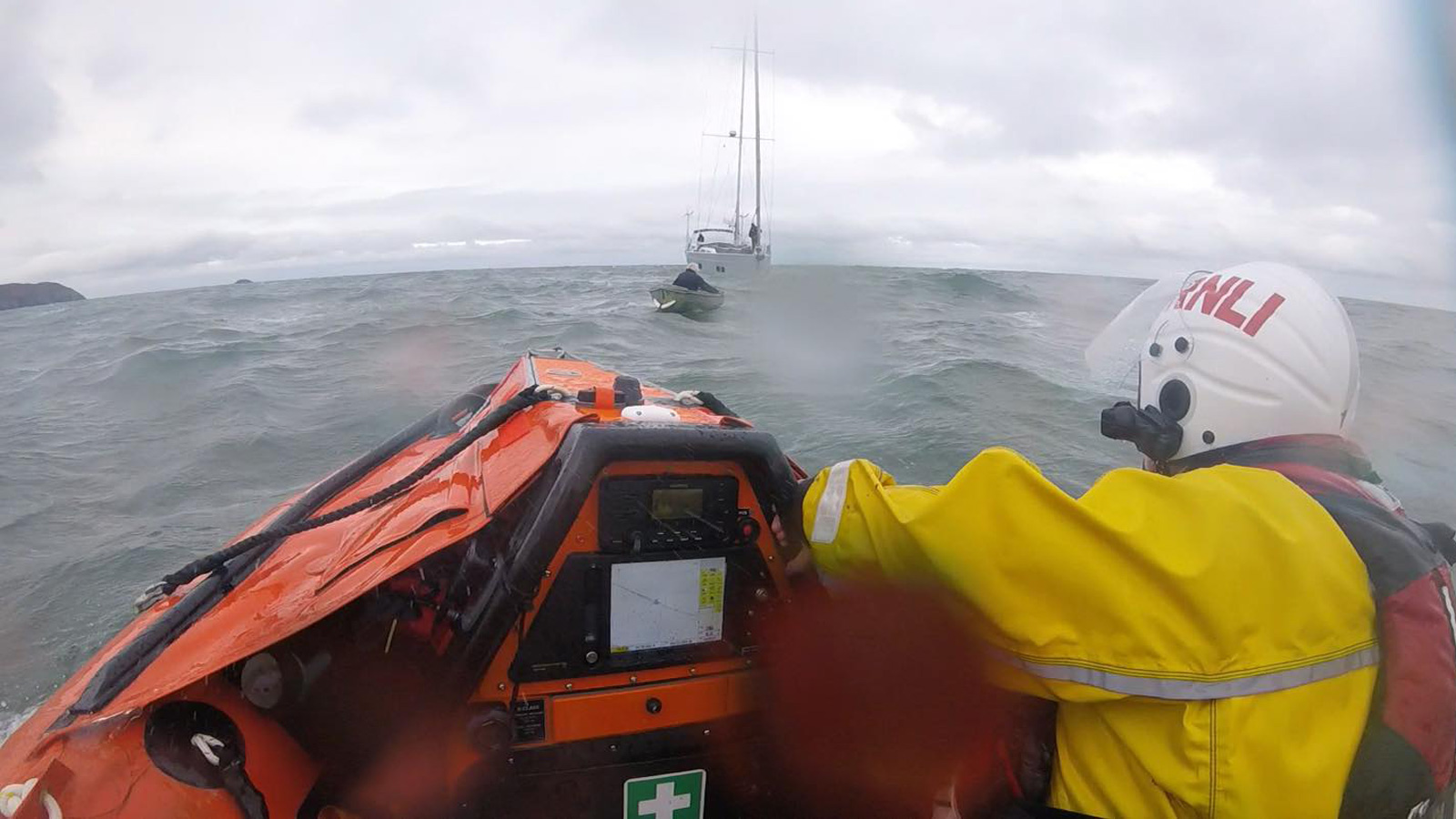 Moelfre lifeboat approach a man in a row boat being towed by a yacht