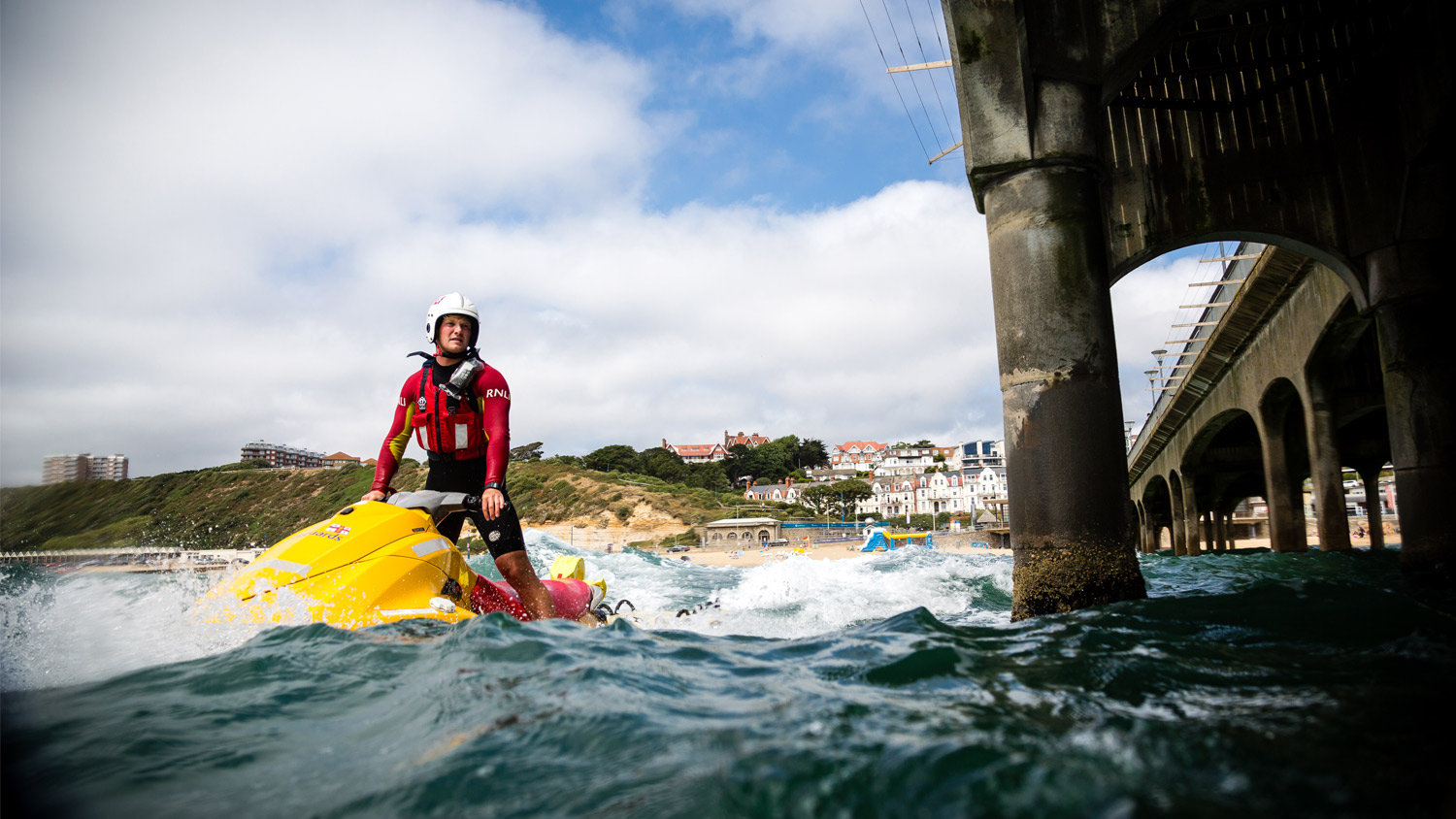A lifeguard wearing a helmet onboard a rescue watercraft next to a pier