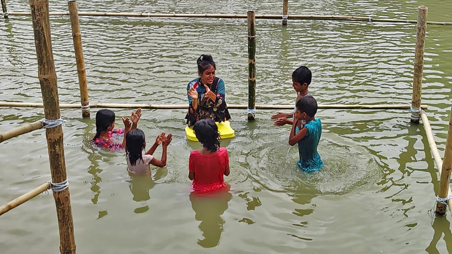 Five children and their swimming instructor stand in the water, learning how to swim