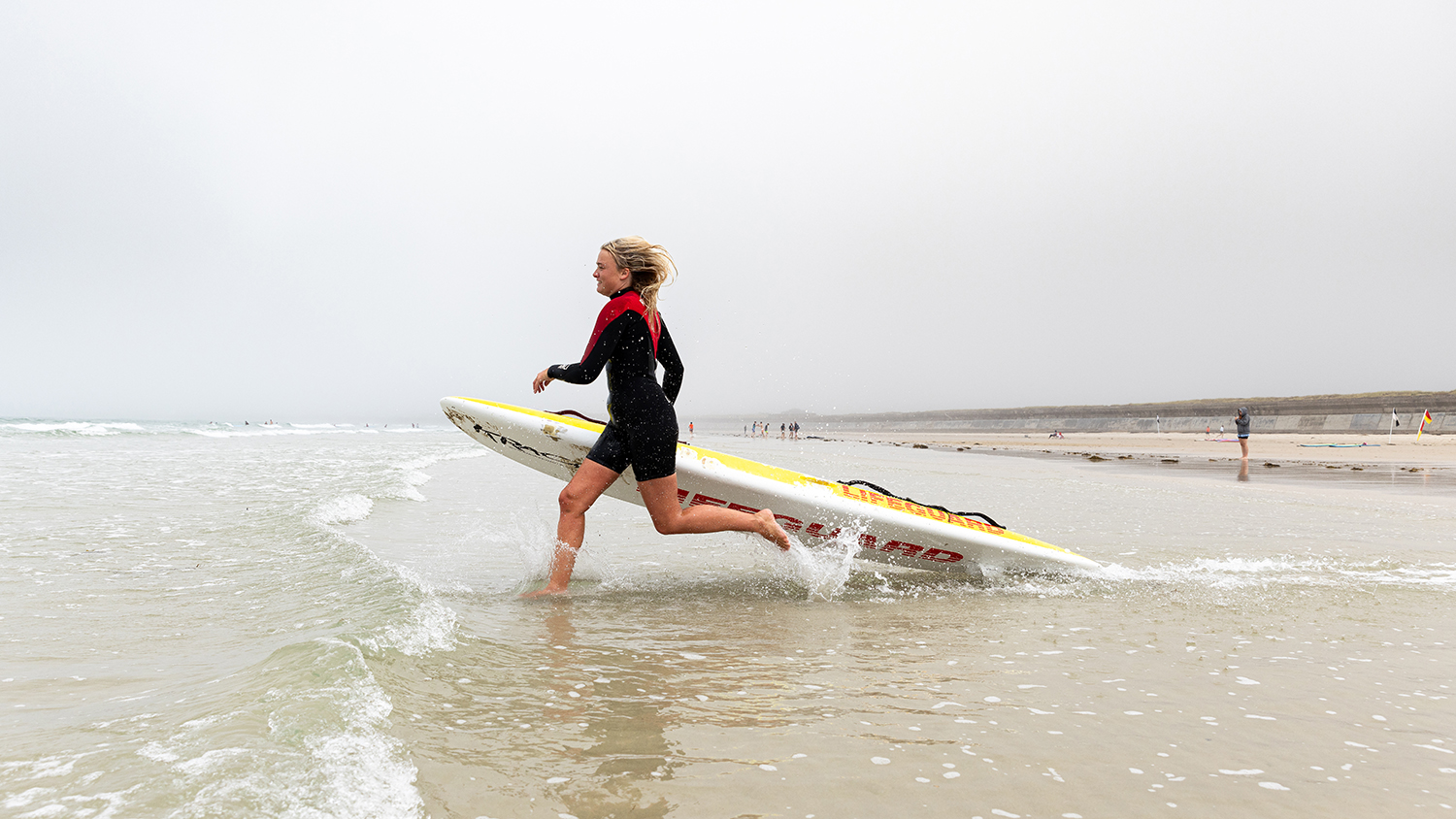 RNLI Lifeguard Jess Collins runs into the sea with a rescue board