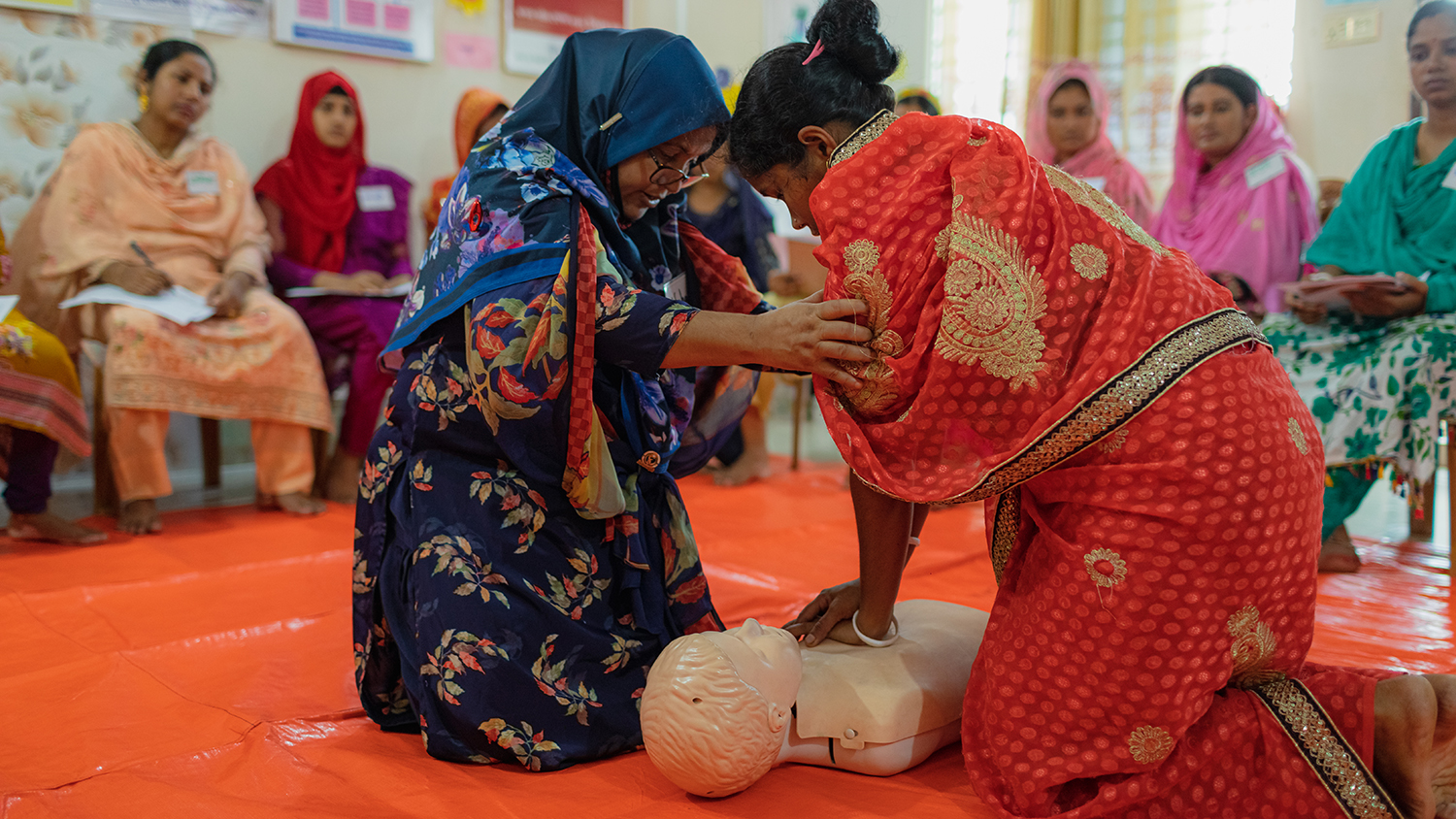 Two women in Bangladesh are learning to perform CPR on a dummy 