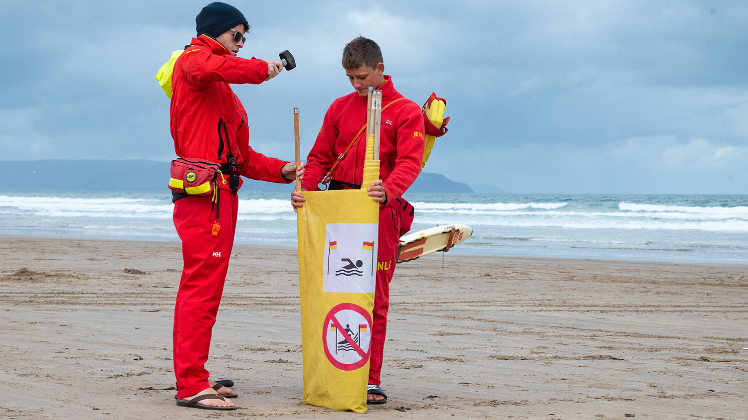 Two RNLI lifeguards hammer signage into the sand