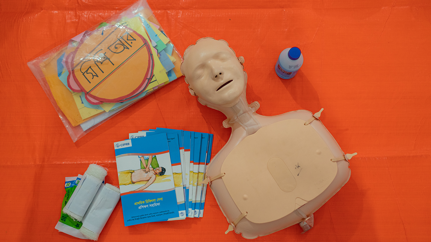 A CPR dummy and leaflets arranged on an orange floor