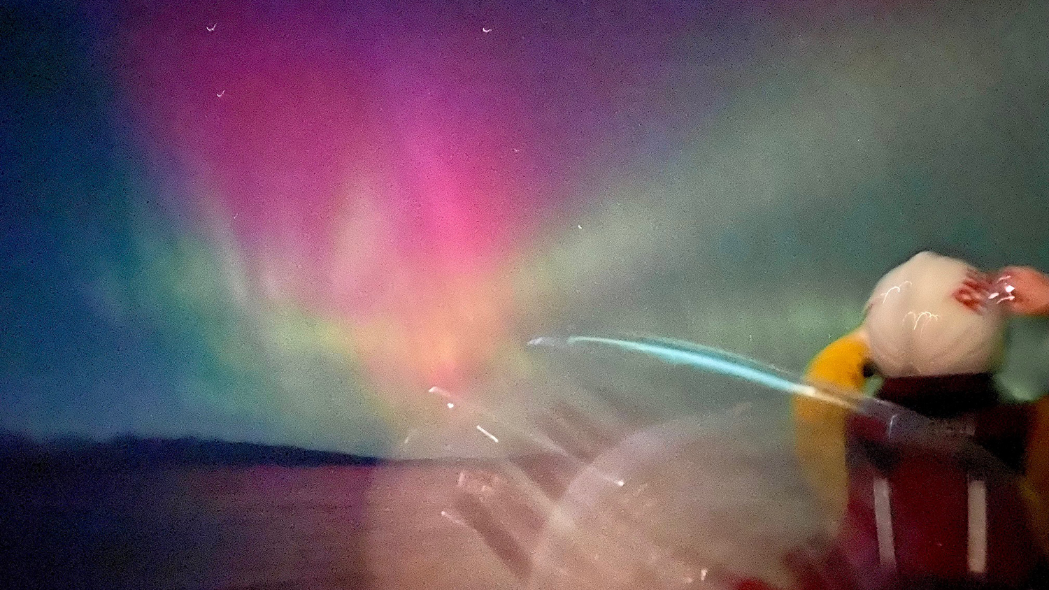 Two Kyle RNLI crew members look towards the blue, pink and green sky of the northern lights