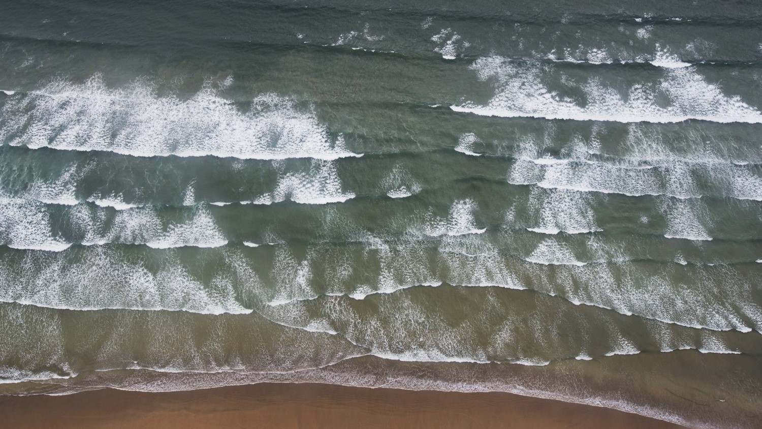 The flatter channel of water in between the white breaking waves at the centre of this photo is a rip current