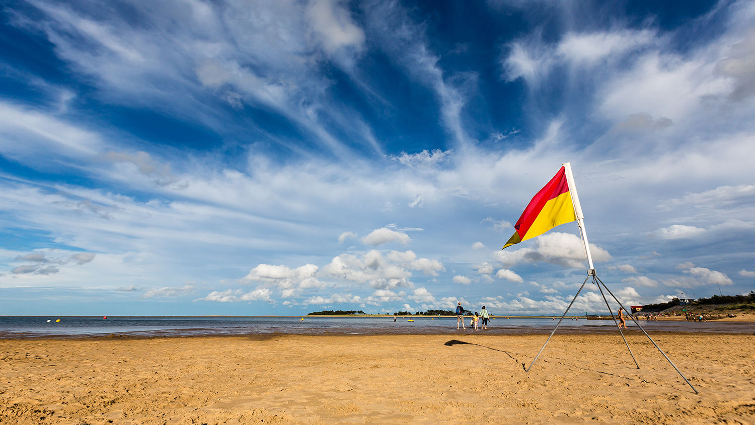 A red and yellow flag on the beach, with lots of blue sky