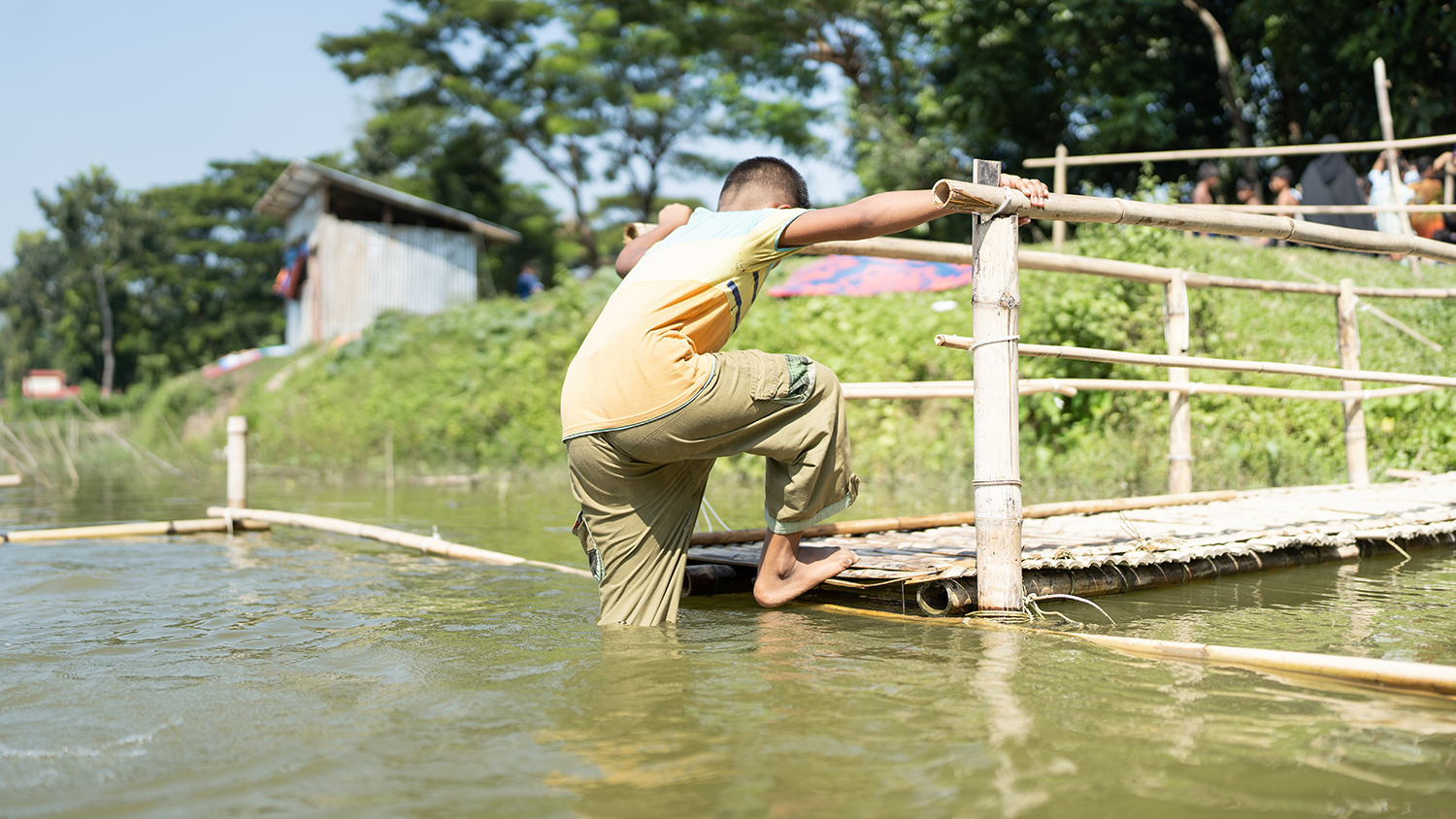 A child climbs down a bamboo structure into the water, taking part in SwimSafe, in Bangladesh