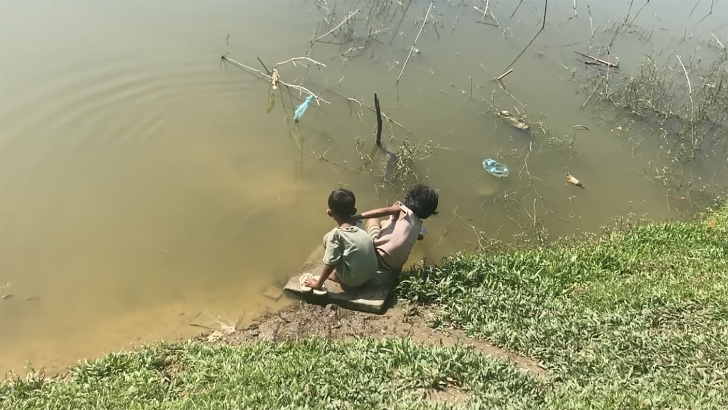 Two children sit at the edge of a pond in Bangladesh