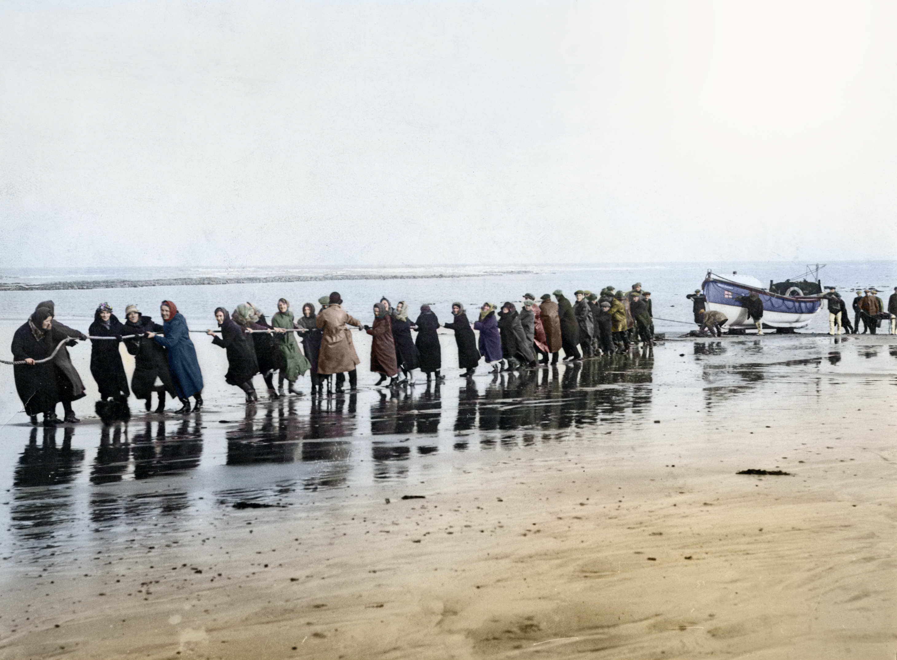 A group of women pulling a vintage lifeboat from the sea using ropes