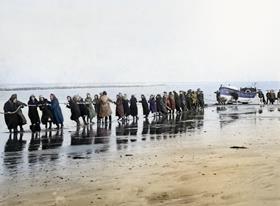A group of women pulling a vintage lifeboat from the sea using ropes