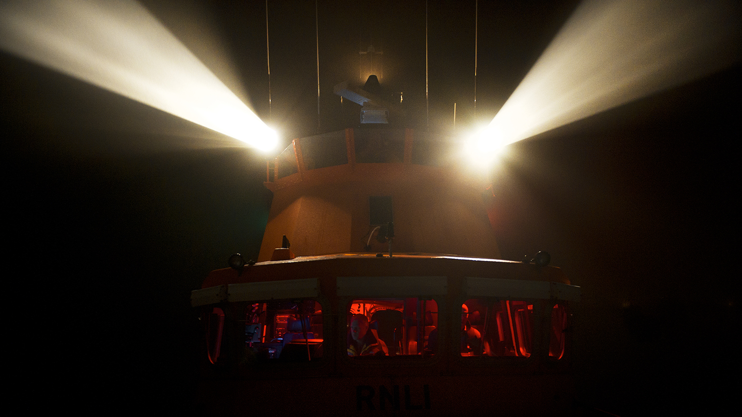 The searchlights of an all-weather lifeboat beam through the pitch black night