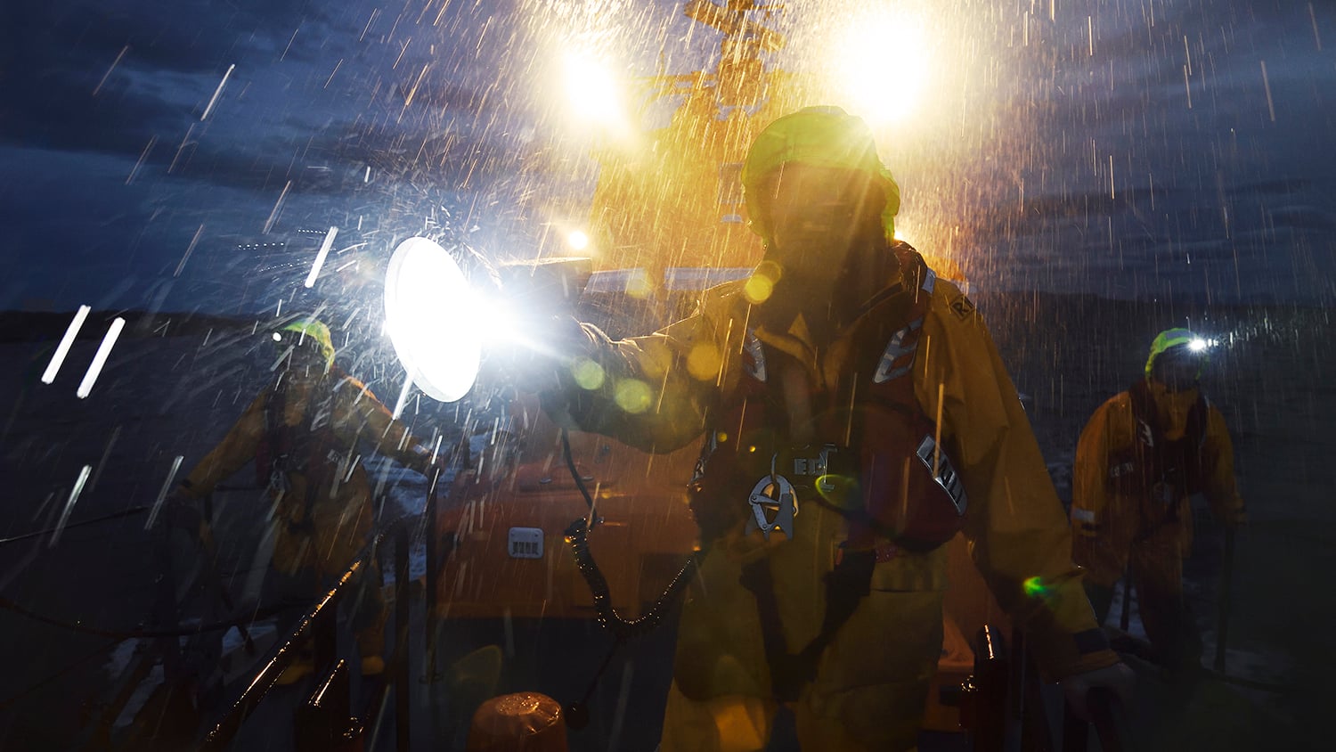 RNLI crew on the deck of their lifeboat, in the dark and heavy rain